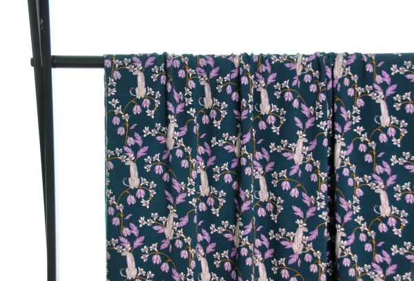 Fast viscose med hvide pumaer, der sidder på grene med lilla blade og lilla og hvide blomster vist draperet over stang og fra afstand