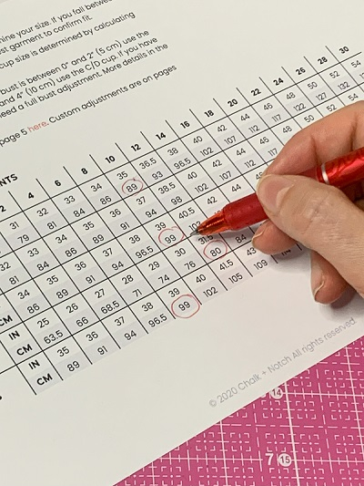 Måleskema med mål i tommer og centimeter for forskellige størrelser, hvor en hånd holder en rød kuglepen, og hvor der er sat røde cirkler rundt om forskellige mål i tabellen.