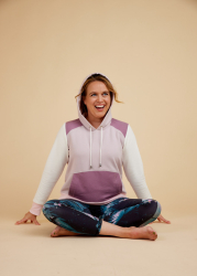 Kvinde med hættetrøje i flere faver i yogaposition med afslappet smil