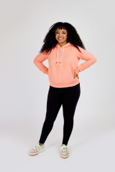 Kvinde i orange hættetrøje og sorte leggings smiler.