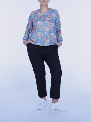 Kvinde i blomstret bluse og sorte bukser på hvid baggrund.