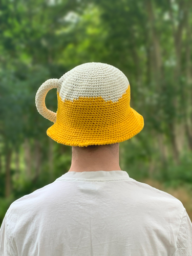 Hæklet øl bøllehat opskrift - hæklet bøllehat i gul og hvid med hank på siden. Den ligner et ølkrus med øl og hvidt skum, der løber ned ad siden på glasset.