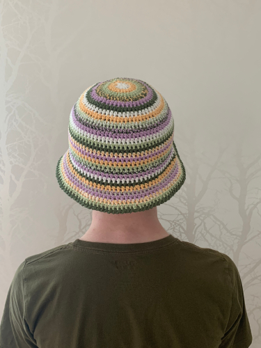 Hæklet bøllehat i grøn, lilla, hvid og lys orange på hovedet af en mand set bagfra.