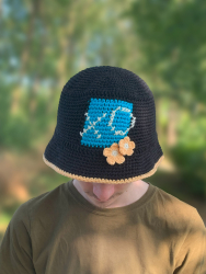 Opskrift på sort bøllehat med turkis firkant på forsiden og et broderet X og et O og blomster.